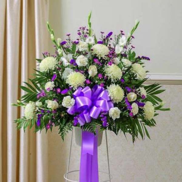 Standing spray of white and purple flowers with a large purple bow on a metal stand
