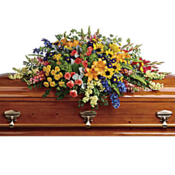 Bright mixed flower casket spray in yellow, orange, blue, and pink on a polished wooden casket