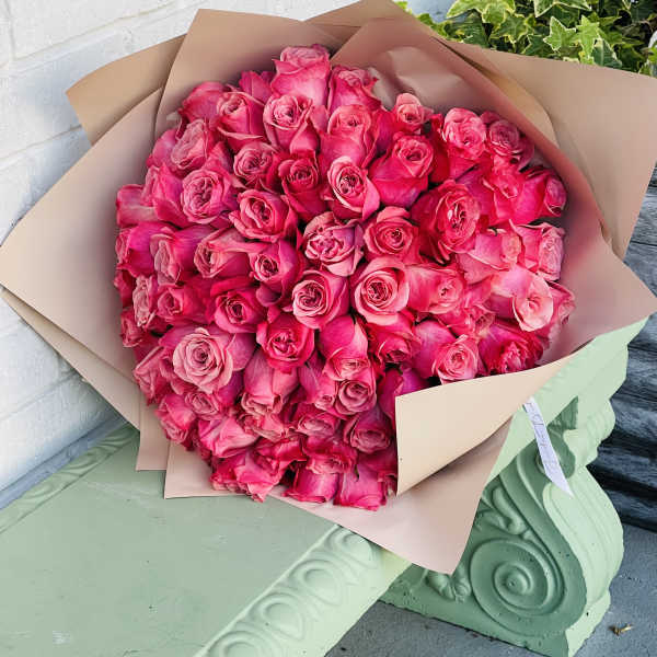 Large bouquet of bright pink roses wrapped in tan paper