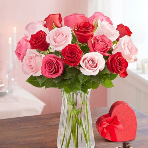 Bouquet of pink and red roses in a clear glass vase with a heart-shaped gift box