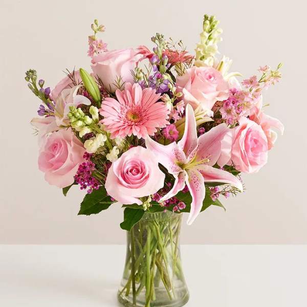 Pink roses, lilies, and mixed blooms arranged in a clear glass vase