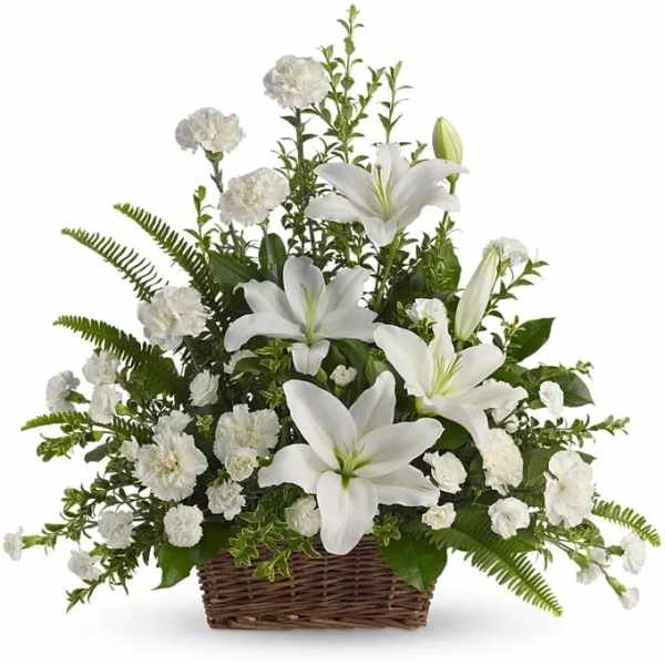 White lilies and carnations arranged in a wicker basket with abundant foliage