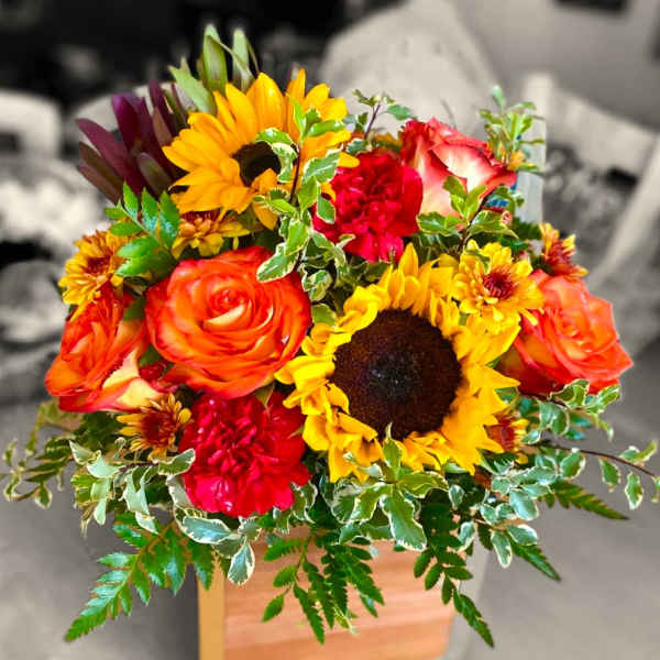 Bright mixed bouquet with sunflowers, roses, and carnations in a wooden box