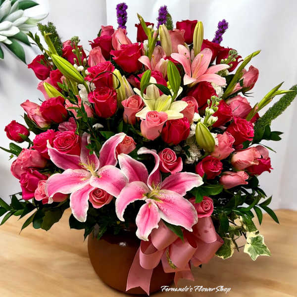 Large arrangement of pink lilies and mixed pink and red roses in a brown bowl vase
