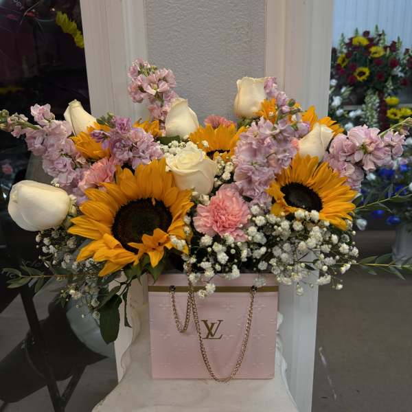 Bouquet of sunflowers, white roses, and pink flowers in a pink gift bag