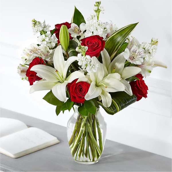 Vase arrangement of white lilies and red roses with white accent flowers in a clear glass vase