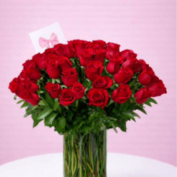 Tall clear vase filled with many red roses and a small card on a white table