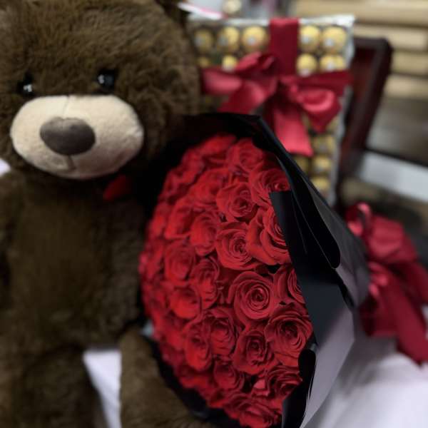 Teddy bear beside a bouquet of red roses and a gift box with a ribbon