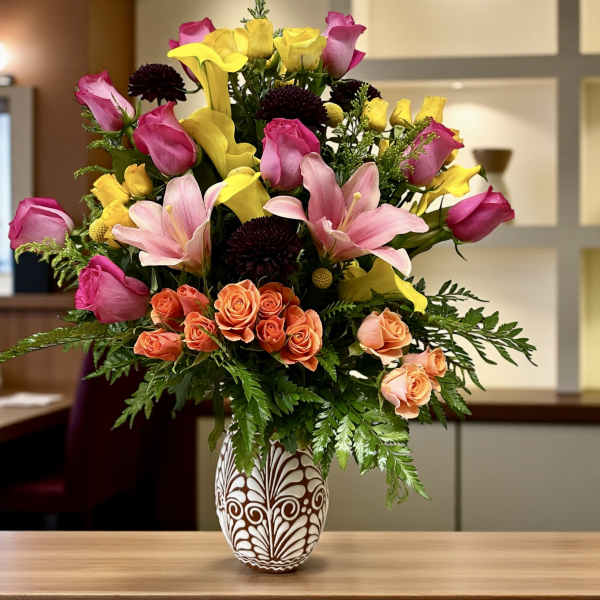 Mixed bouquet of pink roses, yellow callas, and lilies in a patterned vase