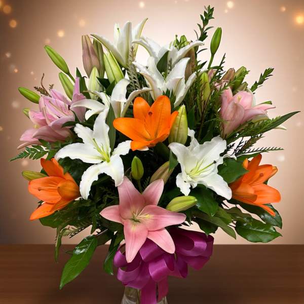 Bouquet of white, pink, and orange lilies in a glass vase with a purple ribbon