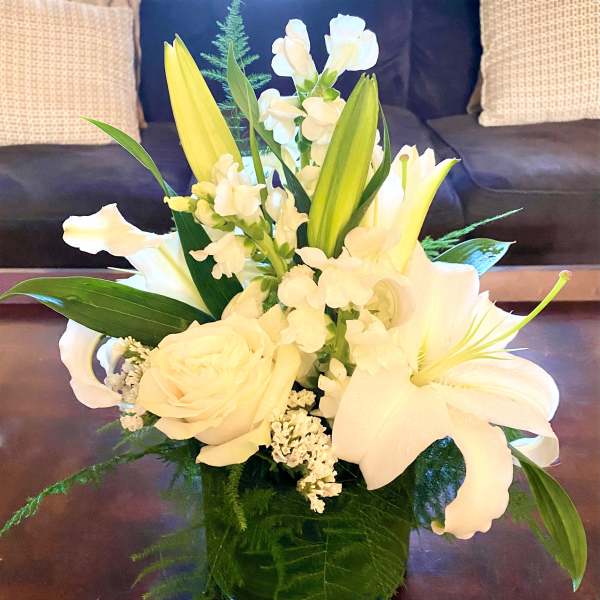 White lilies and roses in a glass vase with green foliage
