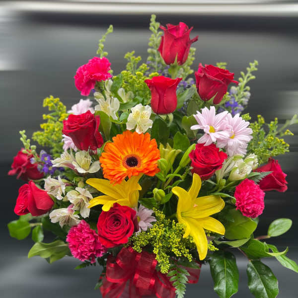 Mixed arrangement of red roses, yellow lilies, pink carnations and orange gerbera in a pink vase