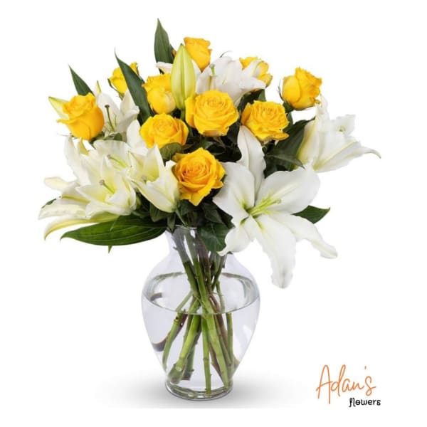 Yellow roses and white lilies arranged in a clear glass vase