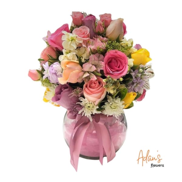 Mixed pink and yellow rose bouquet in a glass vase with a pink ribbon