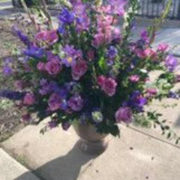 Large purple and pink floral arrangement in a pedestal vase outdoors