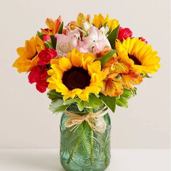 Bouquet of sunflowers, lilies, and carnations in a green glass jar
