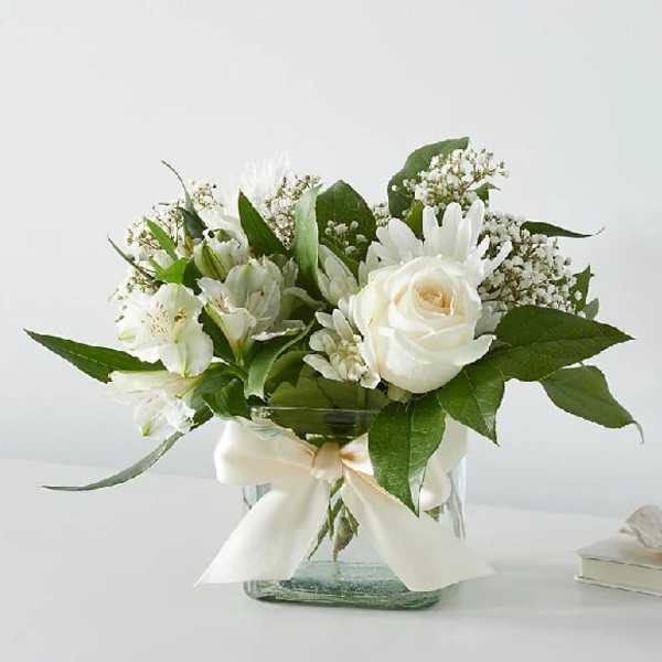 White roses and lilies arranged in a glass vase with a ribbon