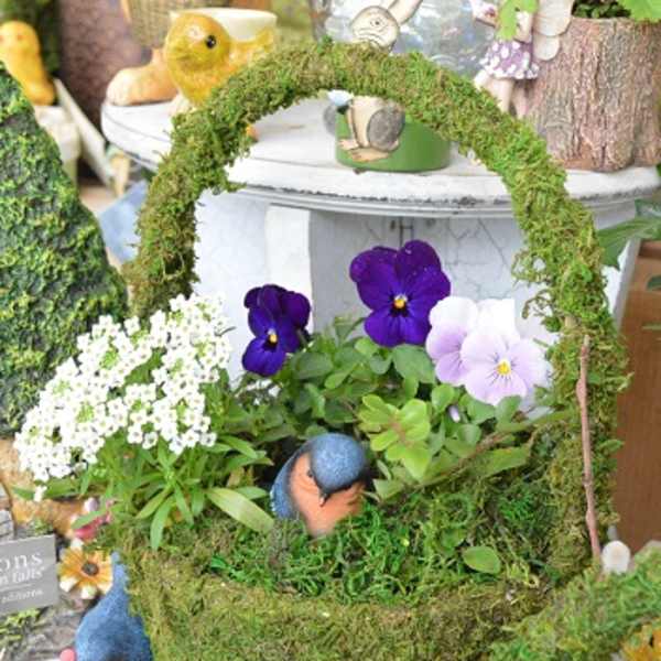 Moss-covered basket with purple and white pansies and small bird figurines
