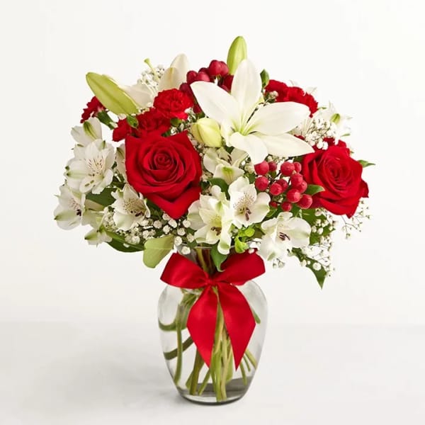 Red roses and white lilies in a clear glass vase with a red ribbon