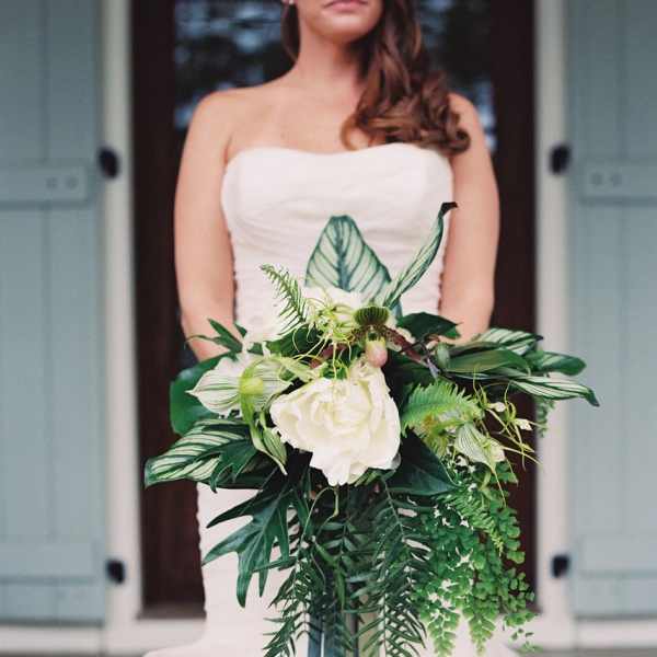 Bride holding a white bouquet with lush green foliage and long ribbon streamers