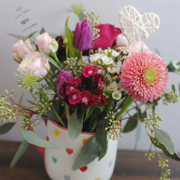 Mixed pink and purple flower arrangement in a heart-patterned mug