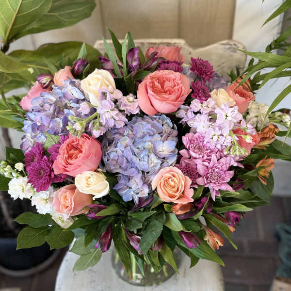 Bouquet of pink roses, blue hydrangea, and purple flowers in a glass vase