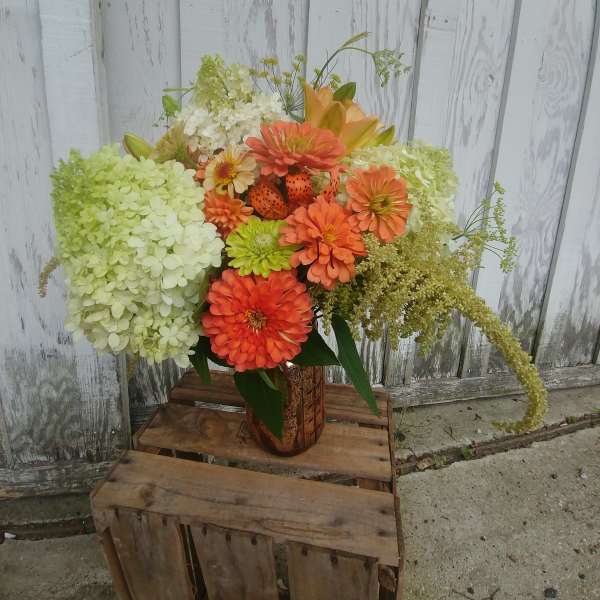 Orange and green floral arrangement in a rustic vase