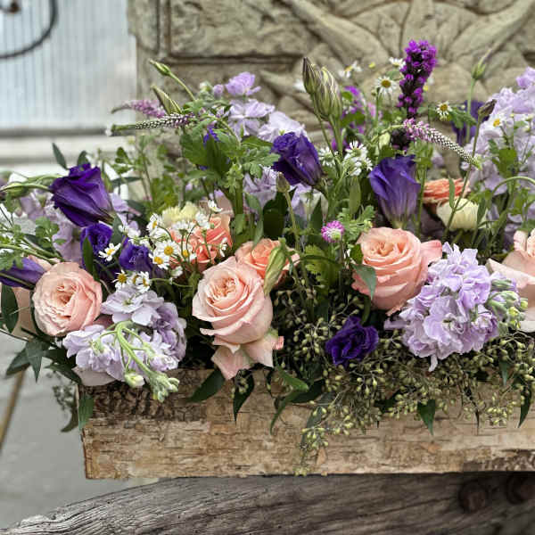Low floral arrangement with peach roses and purple blooms in a wooden box