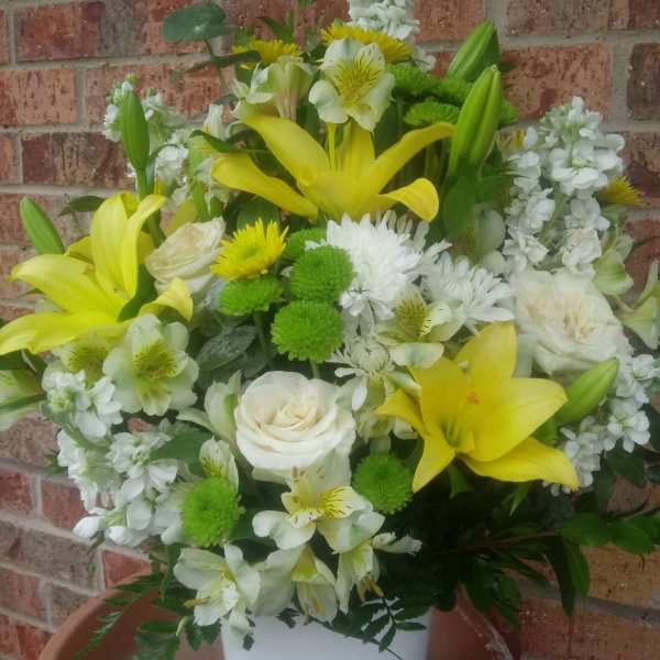 Yellow lilies and white roses arranged in a white vase