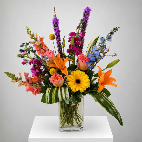 Colorful mixed bouquet in a clear glass vase with orange lilies and yellow gerbera daisies