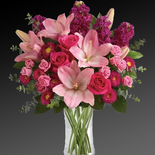 Pink lilies and roses arranged in a clear glass vase