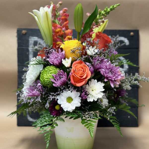 Mixed bouquet in a white vase with lilies, roses, and daisies