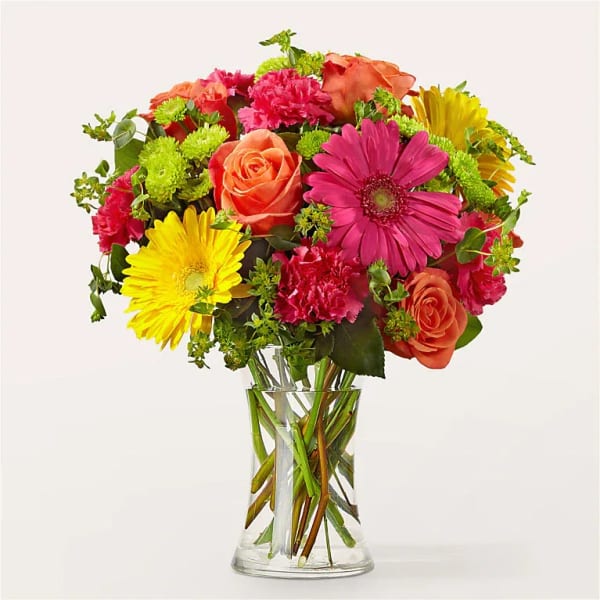 Mixed bouquet of pink, orange, and yellow flowers in a clear glass vase