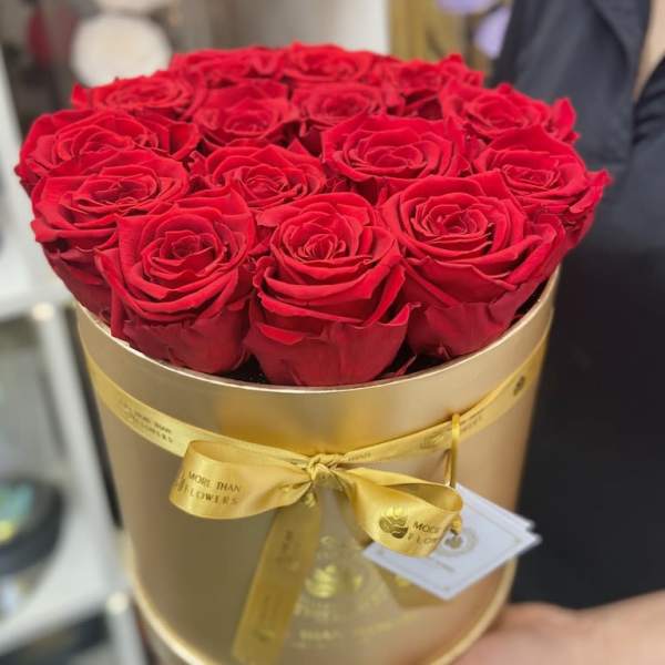 Round gold hat box filled with tightly packed red roses and tied with a yellow satin ribbon