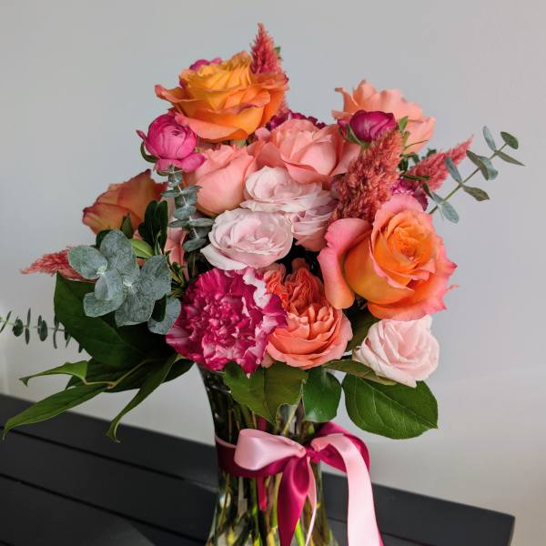 Bouquet of pink and orange roses in a glass vase with a pink ribbon
