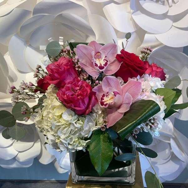 Square vase arrangement with pink orchids, red and hot pink roses, and white hydrangea.