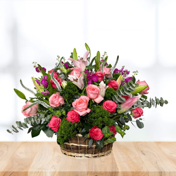 Basket arrangement of pink roses and lilies with purple accents