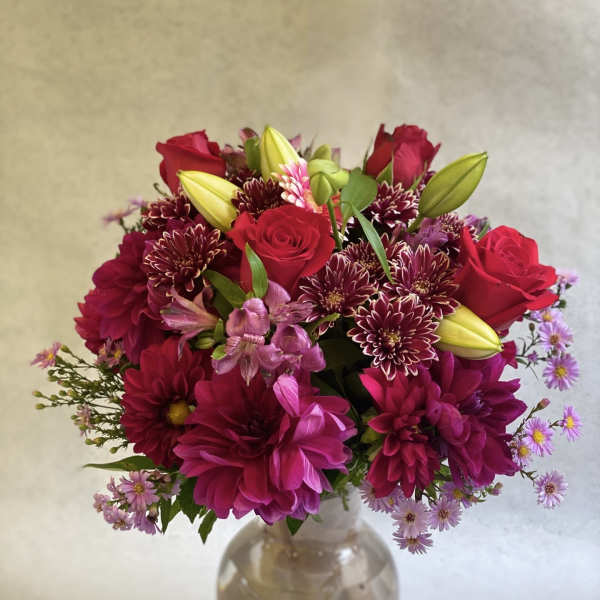 Bouquet of red roses, lilies, and magenta blooms in a glass vase