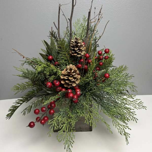 Holiday arrangement of evergreen branches, pinecones, and red berries in a wooden container