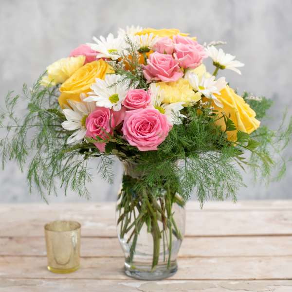 Pink and yellow roses with white daisies in a glass vase
