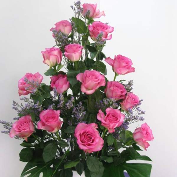 Tall arrangement of pink roses with purple filler flowers in a white vase