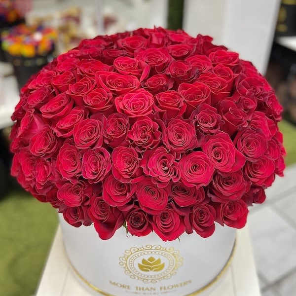Large round box filled with tightly packed bright red roses on a white stand