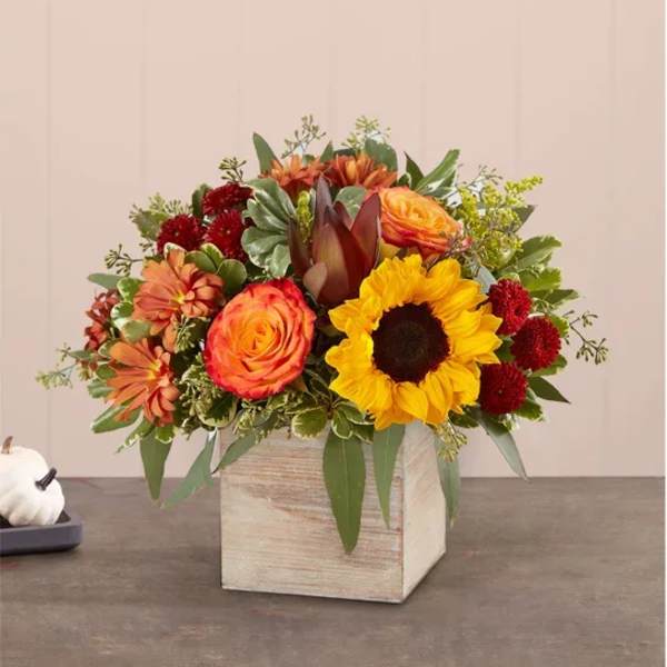 Autumn bouquet with sunflowers, roses, and red blooms in a wooden cube vase