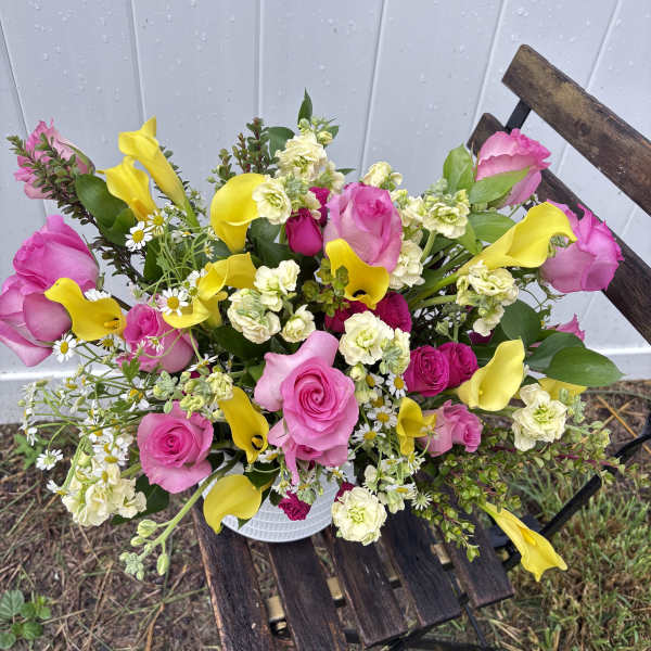 Bouquet of pink roses, yellow calla lilies, and small white flowers in a white container