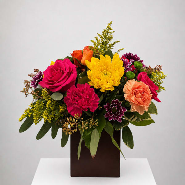 Colorful mixed bouquet in a dark square vase with roses, carnations, and chrysanthemums
