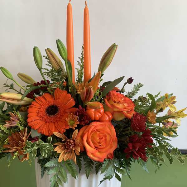 Orange and yellow floral arrangement with two tall orange candles