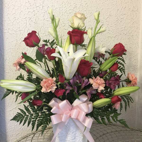 Bouquet of red roses and white lilies in a white vase with a pink ribbon