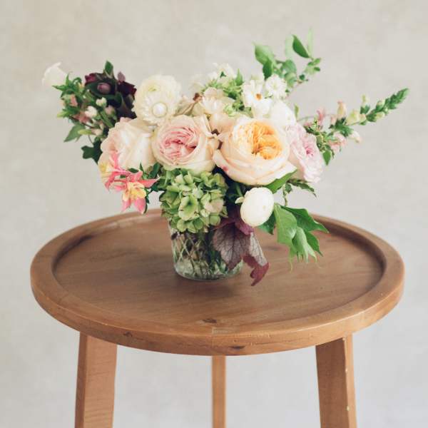 Pastel floral arrangement in a clear glass vase on a wooden table