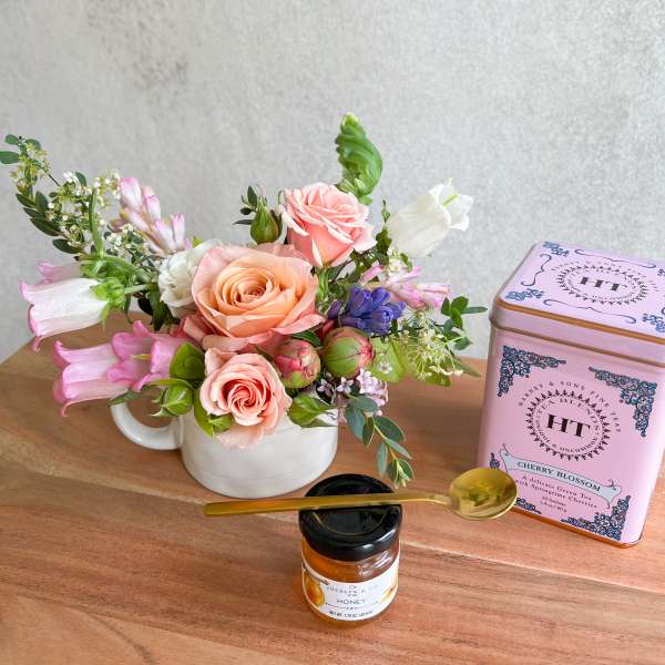 Pink and peach rose arrangement in a white mug with tea and honey gift items