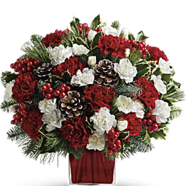 Red and white floral arrangement in a square glass vase with pinecones and berries